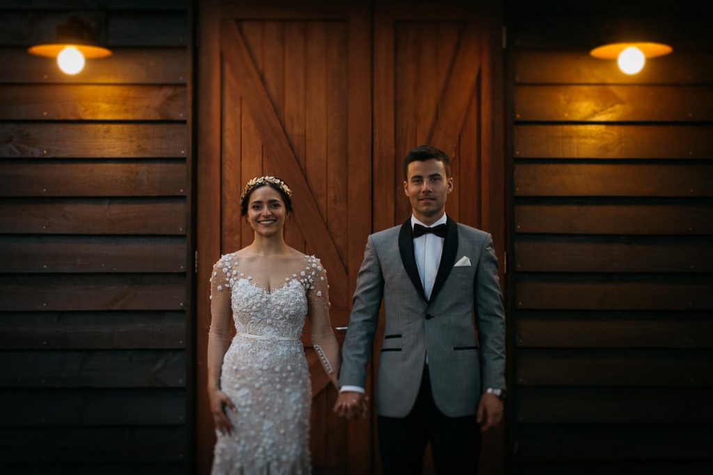 Laura and Daniel hold hands and look at the wedding photography while standing infront of a rustic wooden door; Southern Highlands Wedding Photography, Bendooley Estate