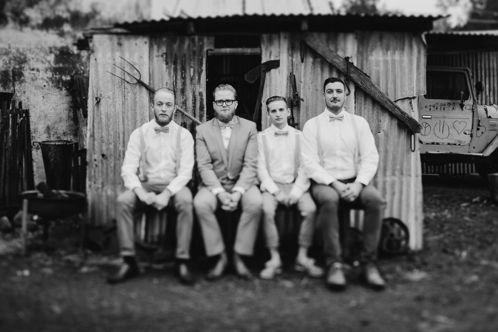 Rustic black and white photograph of groom and groomsmen sitting in front of a tin shed at Jaspers Berry on the South Coast