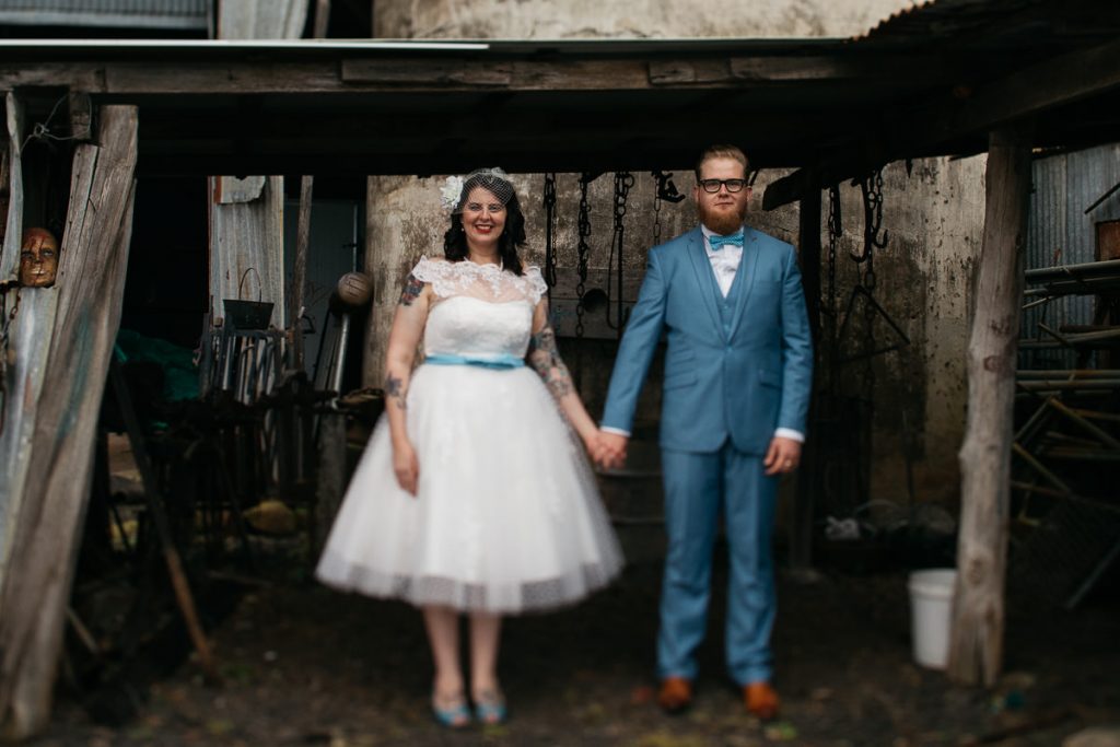 Bride and groom hold hands in a rustc shed while watching the photographer at their Jaspers Berry wedding