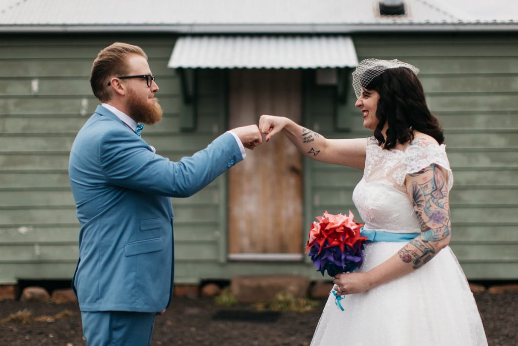 Bride and Groom fist bump in front of a rustic green shed at their Jaspers Berry Wedding on the South Coast