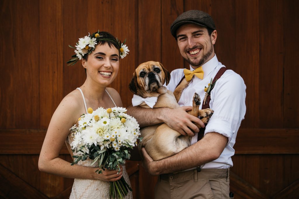 Bride and groom pose laughingly with their dog at their wedding in Berry on the South Coast