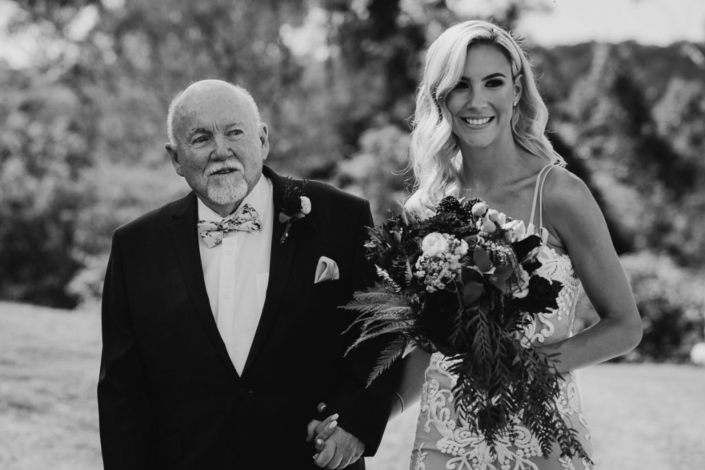 Black and white wedding photograph of the father of the bride holding his daughter's, the bride, hand at her wedding in Bundanon on the South Coast