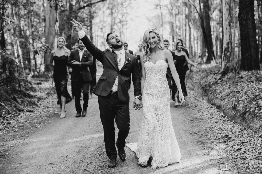 groom raises his hand in celebration while holding his brides hand walking in the forest at Bundanon; black and white wedding photography
