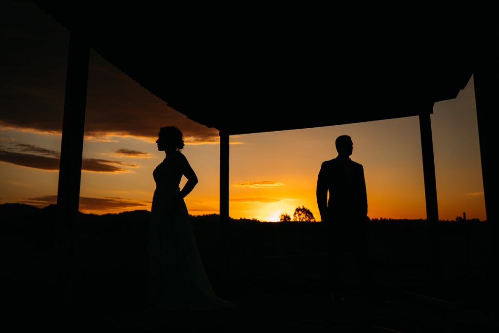 Sunset silhouette photograph of bride and groom standing apart at their Burnham Grove Wedding
