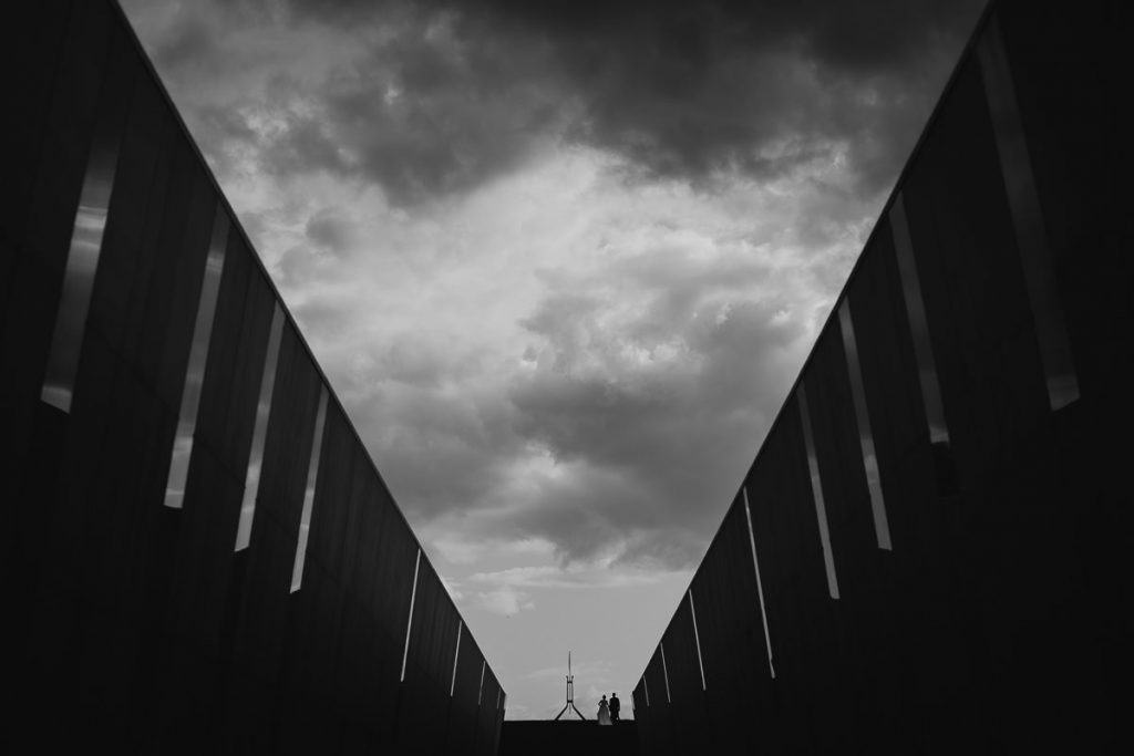 Black and white wedding photograph of a couple walking through the Memorial museum in Canberra