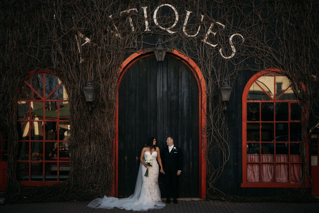 Rustic photograph of a bride and groom standing in the closed arched doorway of an antiques shop at Centennial Vineyards in Bowral