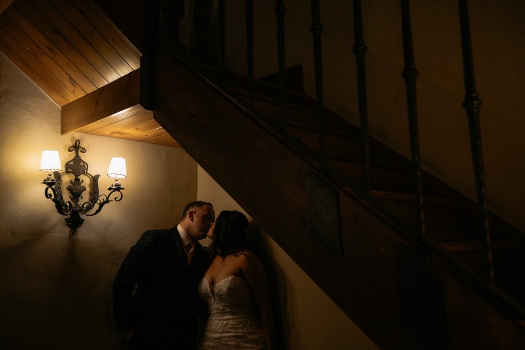 Photograph of a bride and groom sneaking a kiss below the stairs at their Centnnial Vineyards wedding in Bowral