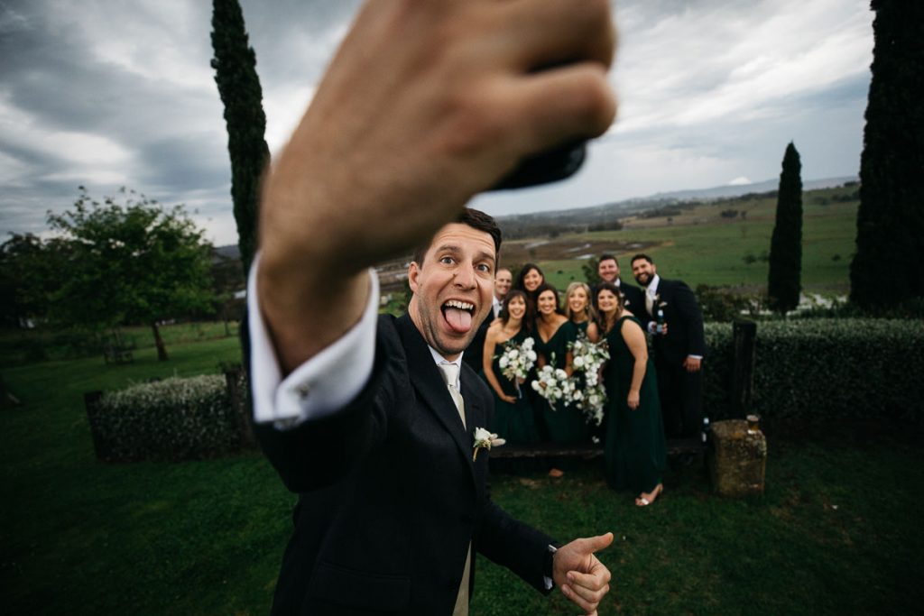 The wedding photographer catches the groom in the act of taking a silly selfie of himself and the wedding party at his Cupitts Winery Wedding
