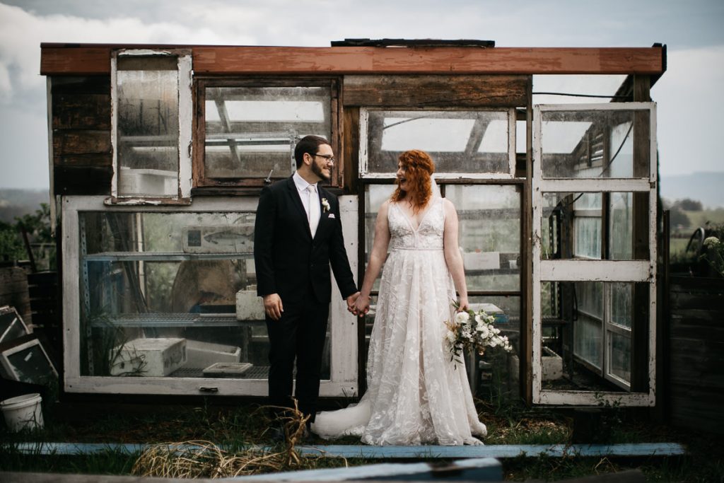 Cupitts Winery Wedding photographer; Southern Highlands: Julie+Steven stand side by side, looking at each other lovingly infront of a rustic hothouse
