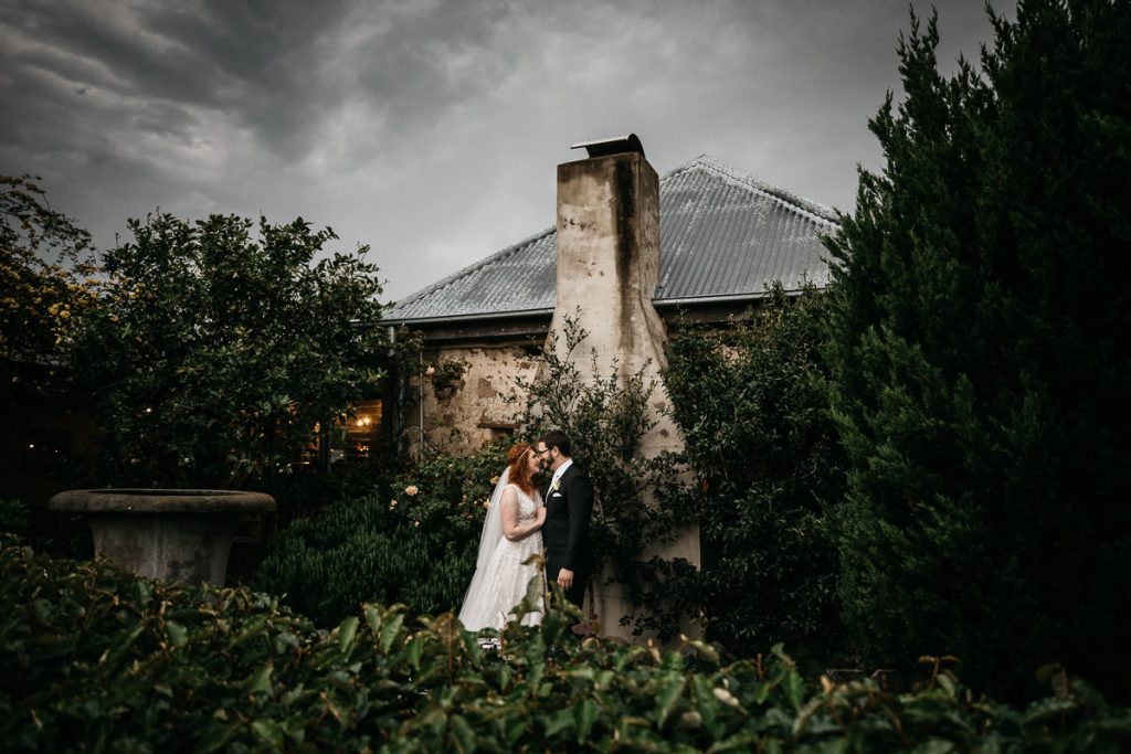 Bride and groom prepare to kiss outside next to the chimney at their Cupitts Winery Wedding; South Coast Wedding Photographer