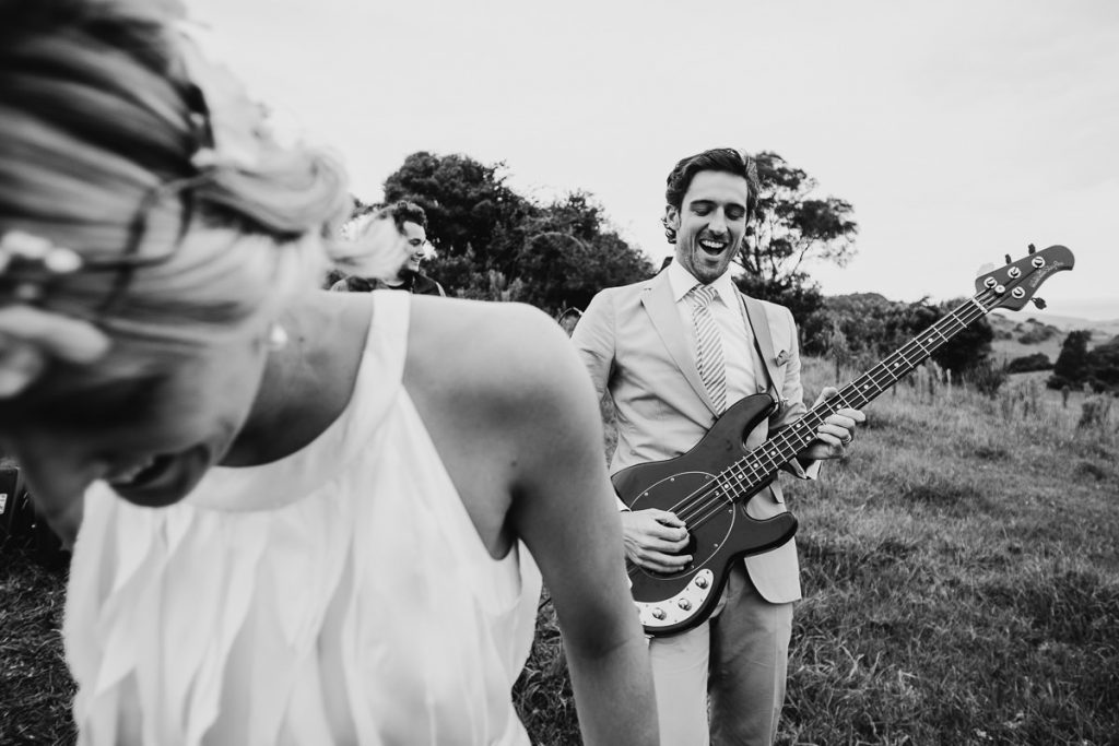 Black and white image of groom playing the fool with an electric guitar while the bride laughs at their wedding at the Mercure in Gerringong