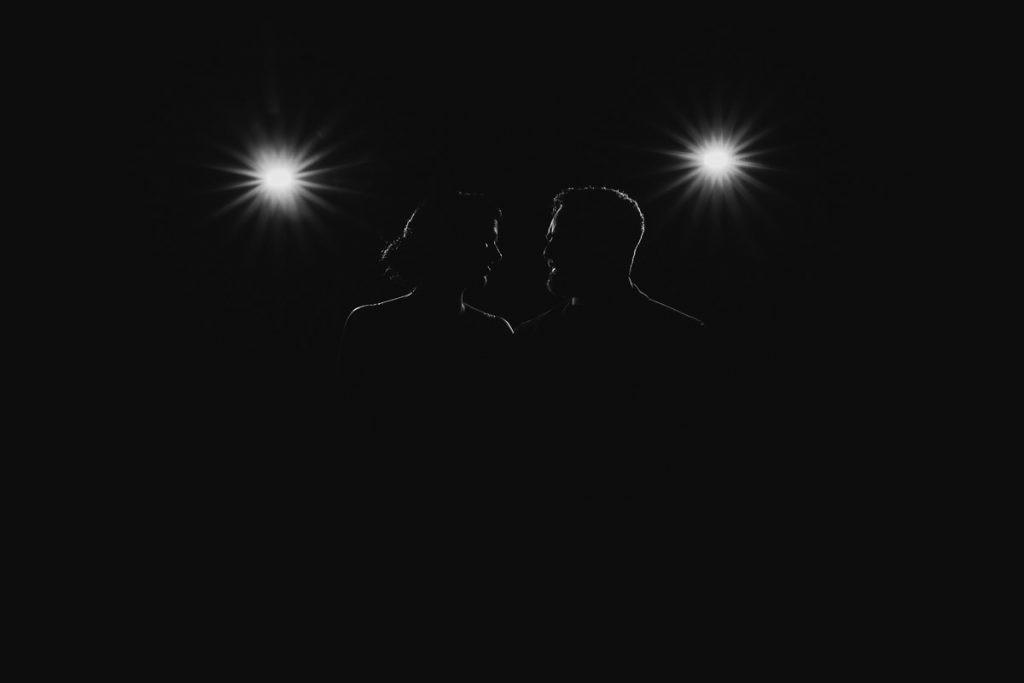 Silhouette of bride and groom looking at each other with lights flashing in the background