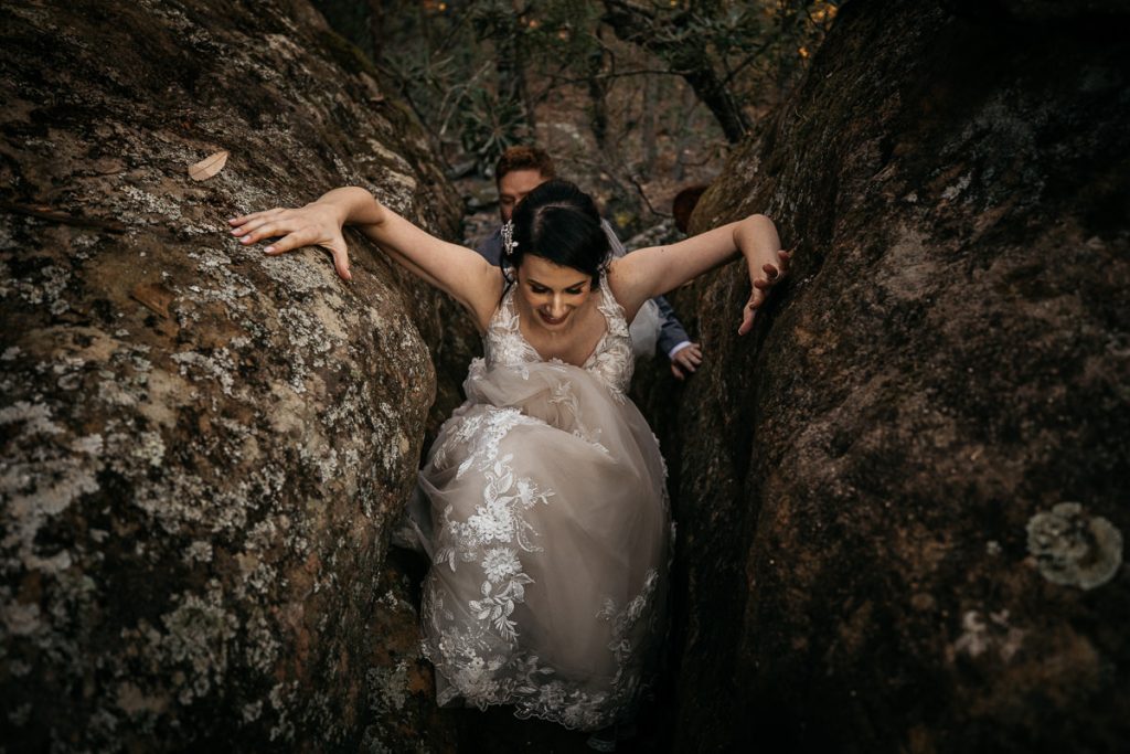 Bride climbs through rocks supported by her newly-wed husband at the Kangaroo Valley Bush Retreat; wedding photography