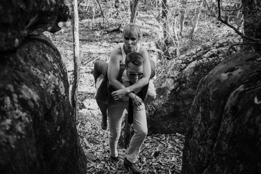 Groom piggybacks his bride through the rocks at their Kangaroo Valley Bush Retreat Wedding; Wedding photographer South Coast