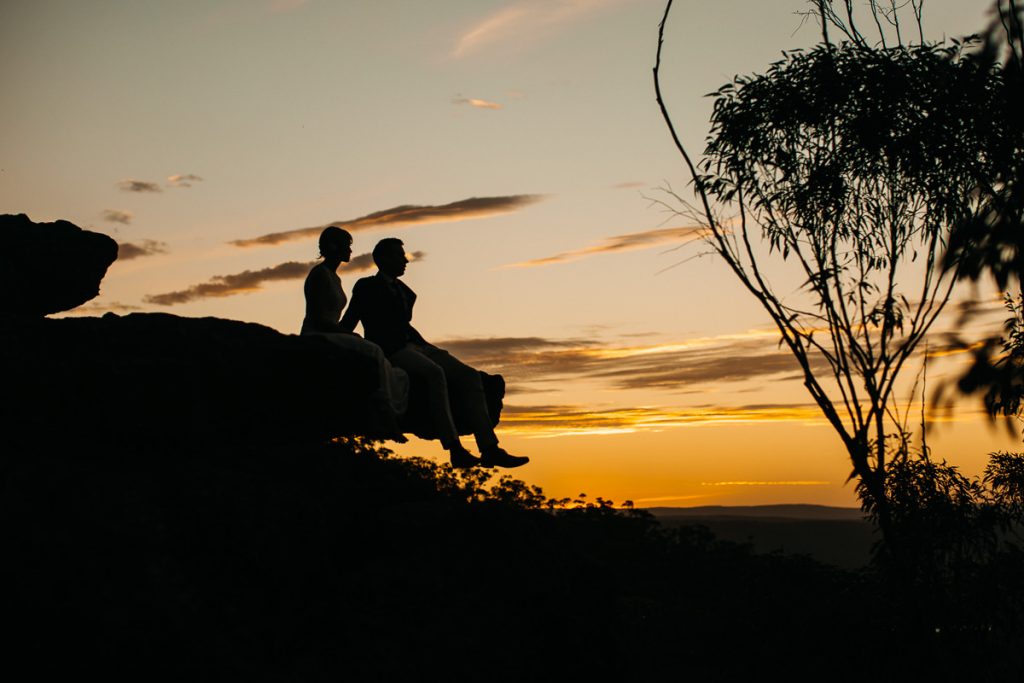 Kangaroo Valley Bush Retreat Wedding Photography; sunset silhouette of bride and groom sitting on an overhanging rock
