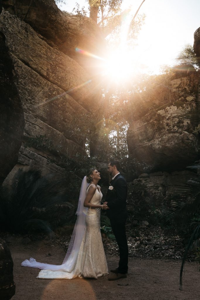 Wedding photograph of couple sharing a joke with the sun shining between the rocks above them