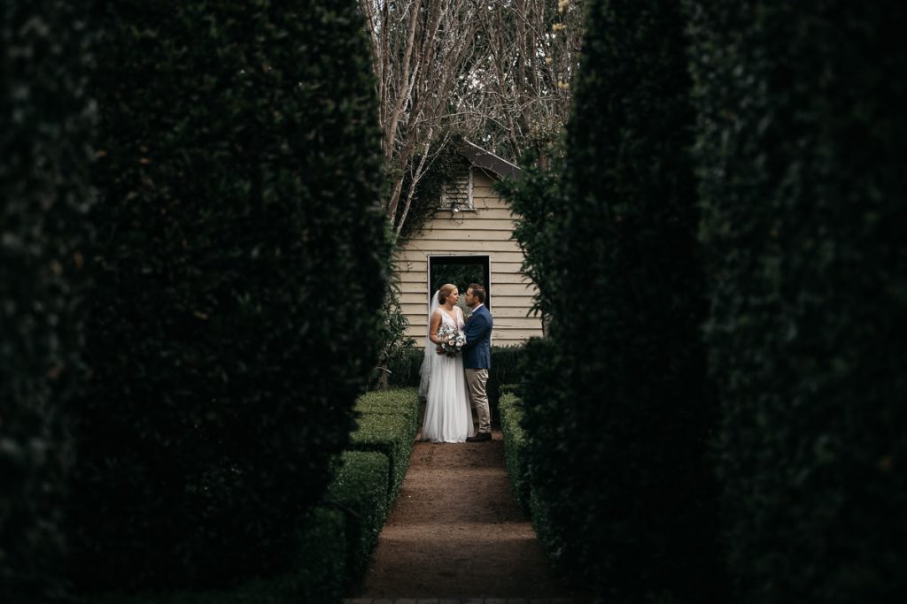 Bride and groom look at each other alng the path between the shrubs at their wedding in Merribee on the South Coast; Wedding Photographer