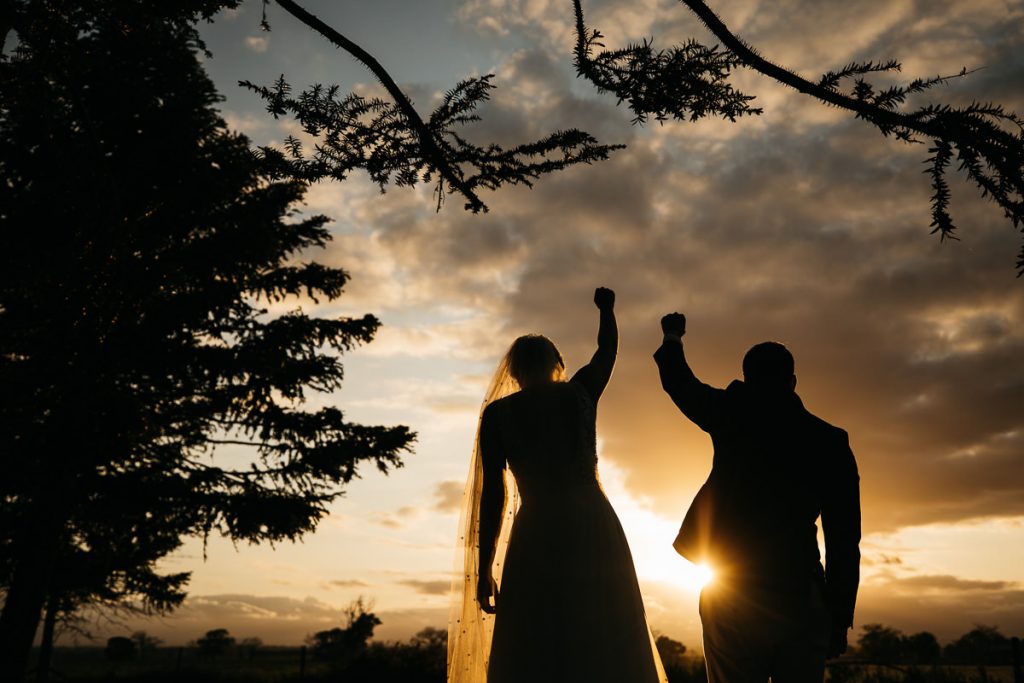 Silhouette of bride and groom pumping their fists in the air at the Merribee wedding; South Coast Wedding Photographer