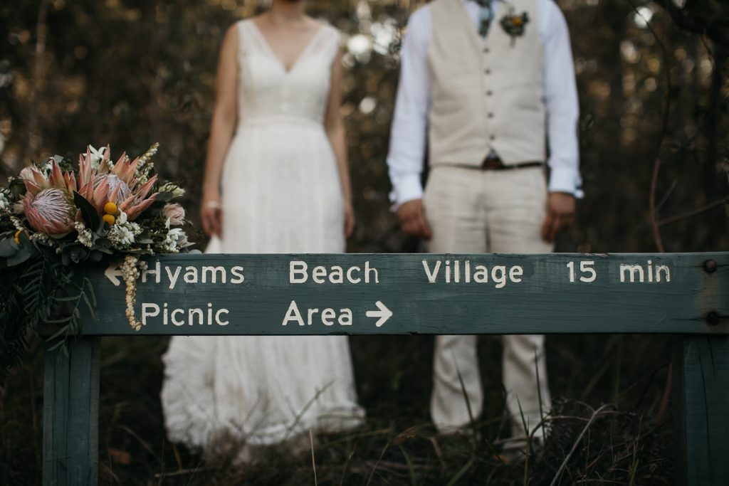 Creative portrait of wedding bouquet and the direction sign with the brdie and groom out of focus in the background at Paperbark Camp; Wouth Coast Wedding Photography