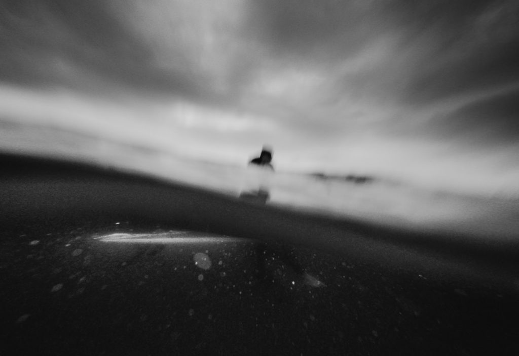 Black and white surfer taken from in the water - groom surfs on the morning of his wedding day; South Coast Wedding photographer