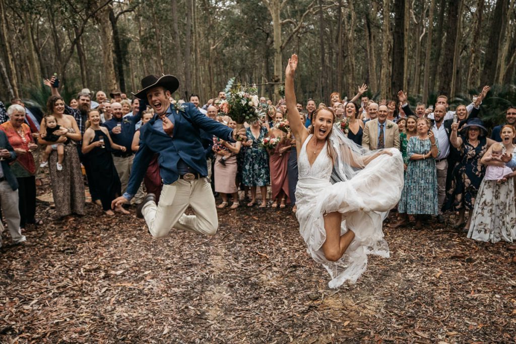 Bride and groom jump for joy in front of their guests; South Coast Wedding Photographer