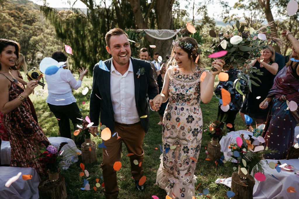 Bride and groom laughingly walk through petal confetti ; Southern Highlands Wedding Photographer
