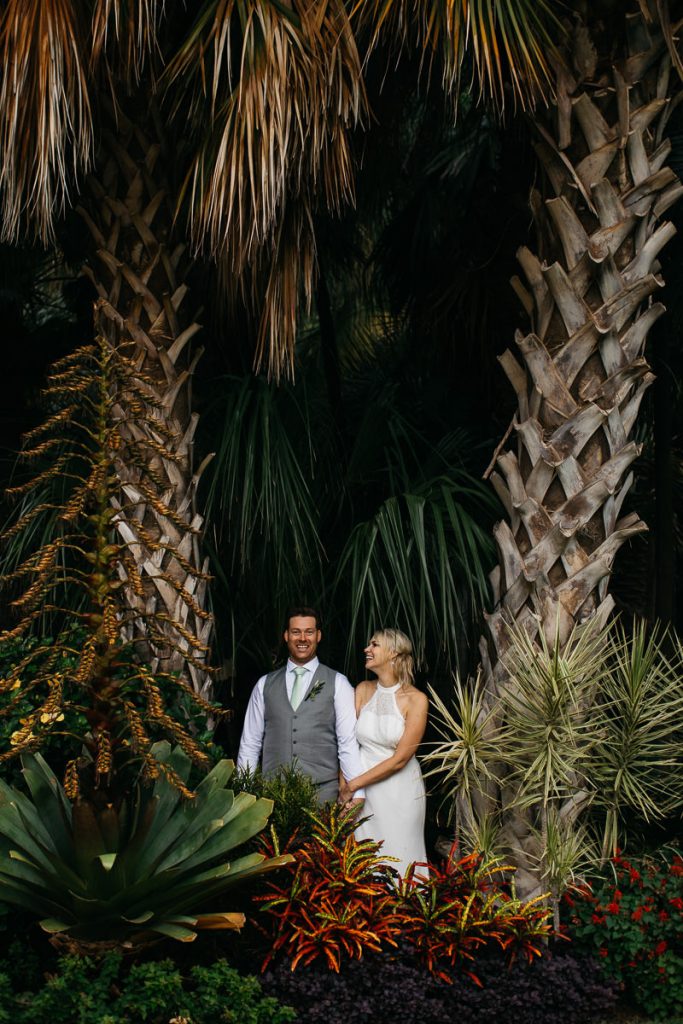 Bride and groom post laughingly between palm trees; Sydney Wedding Photographer