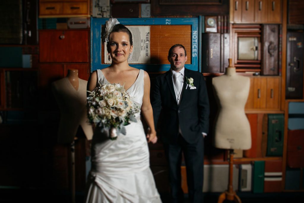 Creative photgraphy of bride pulling groom towards the photographer in a room of wooden boxes and suitcases; Sydney Wedding Photographer