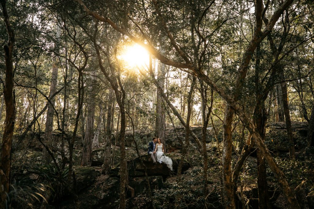 Bridal couple sit on a rock in the middle of the trees at their Wildwood wedding - kangaroo valley wedding photographer south coast