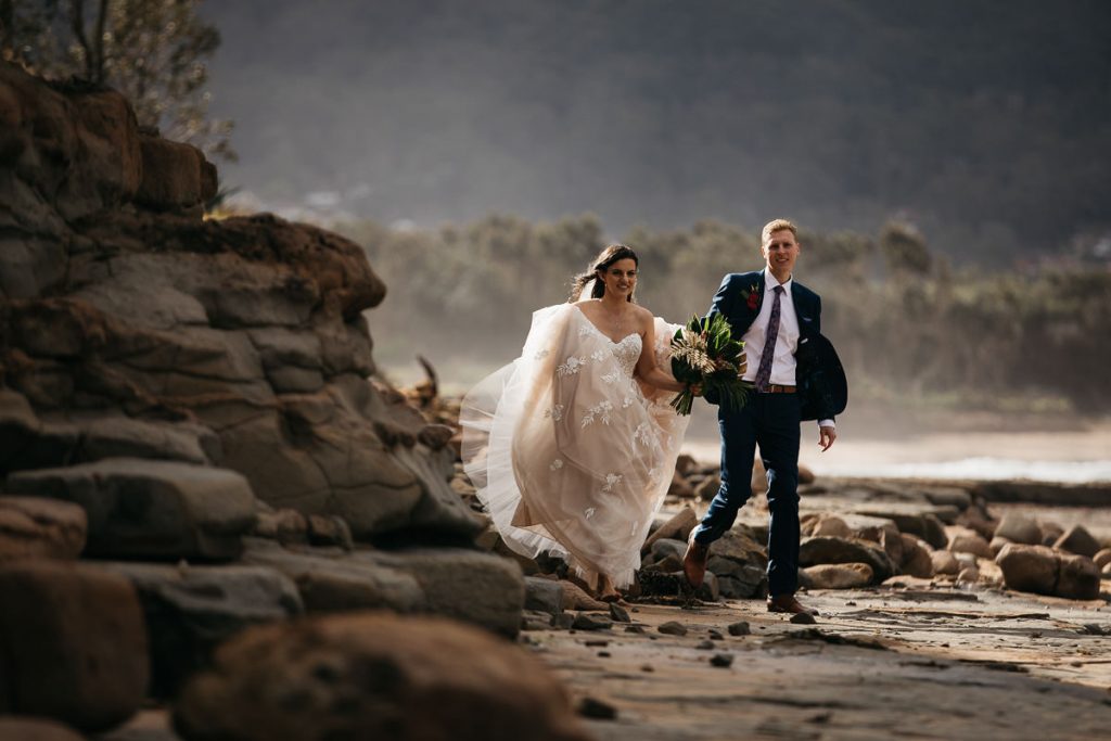 Wollongong wedding photographer; bride and groom walk around the rocks on the beach in Wollongong