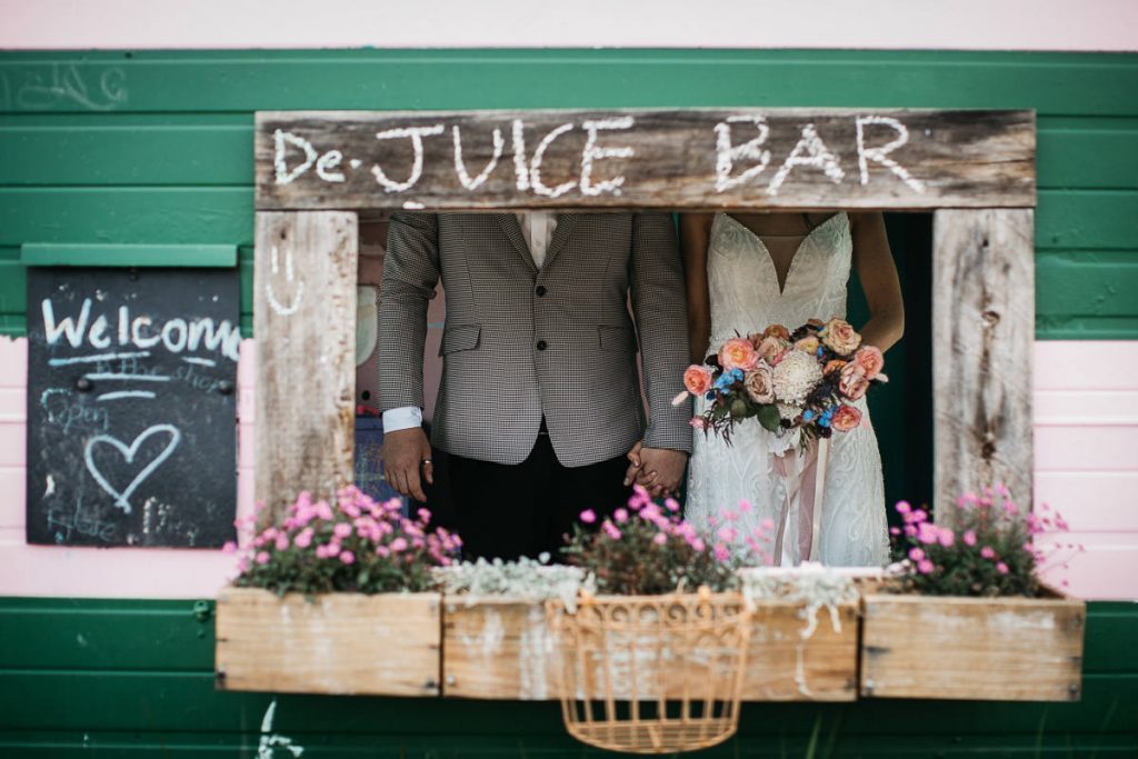 Creative wedding photography; Torso of bride and groom framed by 'De Juice bar' window at their wedding at the Woods Farm on the South Coast