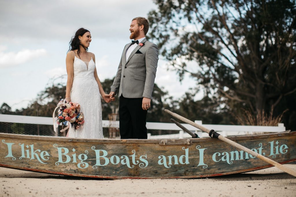 Bride and groom stand in a boat with the words 'I like big boats and I cannot lie' at Woods farm - South Coast Wedding Photographer