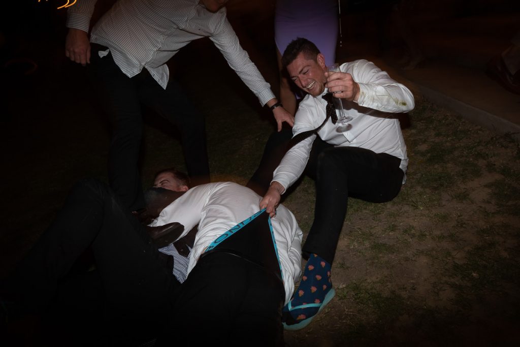 Wedding guests give each other wedgies laughingly at a Woods Farm wedding; Wedding photographer South Coast