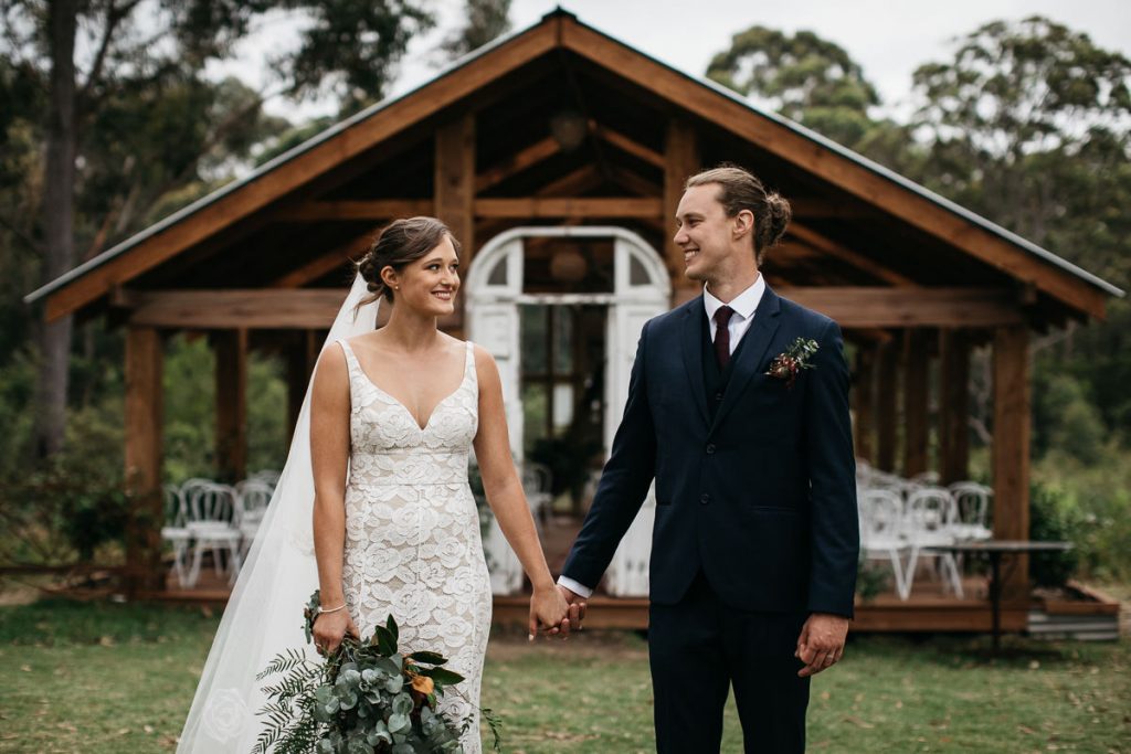 Wedding Couple hold hands and smile at each other in front of their wedding gazebo at their Woods Farm Wedding; Wedding photographer South Coast