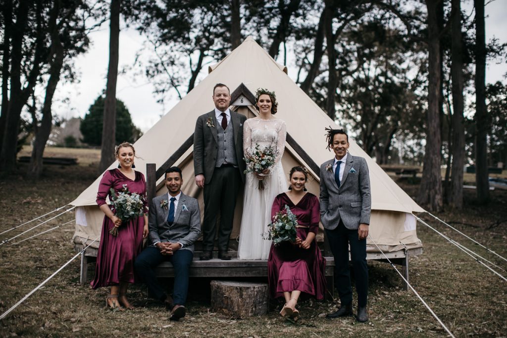 Wedding party group photo taken in front of a triangular white tent